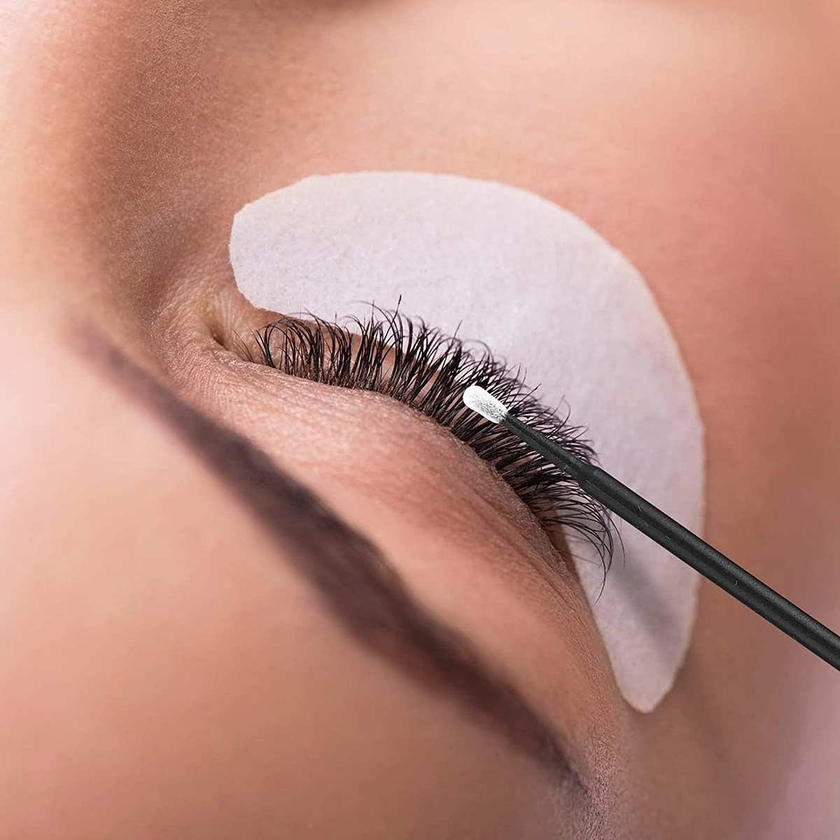 Eyelash artist is using a micro brush to help the customer clean the eyelashes
